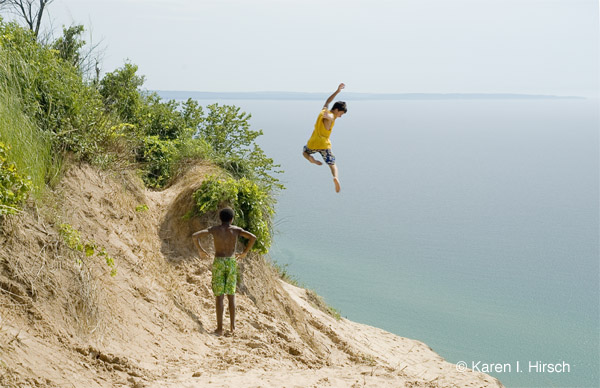 2 boys at sand dunes, one jumping from cliff